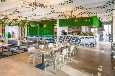 a restaurant with wooden tables and chairs and a green wall at JA The Manor Hotel, Dubai in Dubai