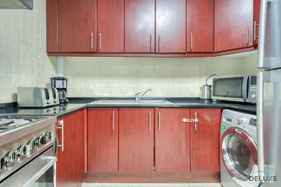a kitchen with wooden cabinets and a washing machine at Community Vibe Living with Wellness Access Close to Metro, Mediterranean, Discovery Gardens by Deluxe Holiday Homes in Dubai