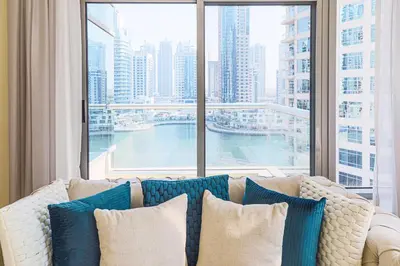 a couch with pillows in front of a large window at Nasma Luxury Stays - Pastel-Colored Apt With Jaw-Dropping Marina Views in Dubai