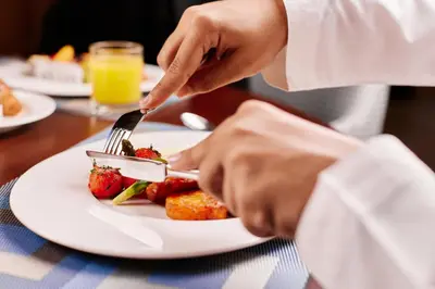 a person eating a plate of food with a fork and knife at Staybridge Suites Dubai Al-Maktoum Airport by IHG in Dubai