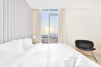 a bedroom with a white bed and a black chair at Posh 2 BR Oceanfront Apt in the Heart of Bluewaters Island in Dubai