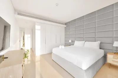 a white bedroom with a white bed and a gray wall at Posh 2 BR Oceanfront Apt in the Heart of Bluewaters Island in Dubai
