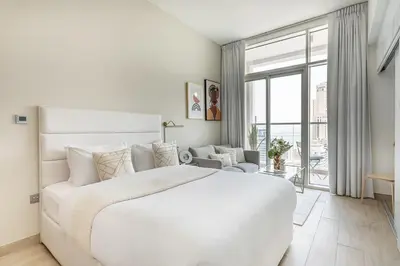 a white bedroom with a large bed and a large window at Frank Porter - Studio One in Dubai