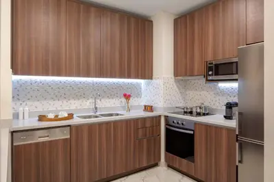 a kitchen with wooden cabinets and a stainless steel refrigerator at Avani Plus Palm View Dubai Hotel & Suites in Dubai