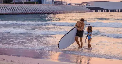 a man and a woman walking on the beach with a surfboard at Jumeirah Beach Hotel Dubai in Dubai