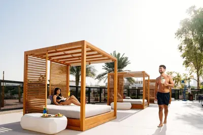 a man and a woman standing on a patio with beds at Rove La Mer Beach, Jumeirah in Dubai