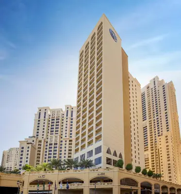 a tall building in front of tall buildings at Amwaj Rotana, Jumeirah Beach - Dubai in Dubai