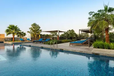 a swimming pool with blue benches and palm trees at Radisson Dubai Damac Hills in Dubai