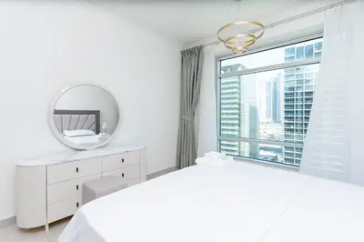 a white bedroom with a mirror and a window at Holidays R Us canal view in Dubai
