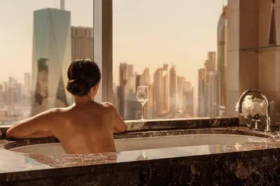 a man sitting in a bath tub looking out a window at Jumeirah Emirates Towers Dubai in Dubai
