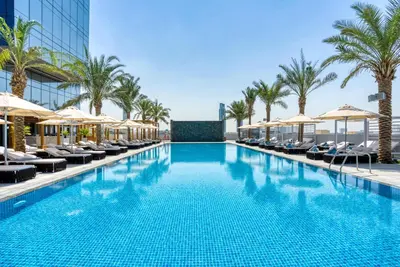 a swimming pool with chairs and umbrellas at a hotel at The First Collection Dubai Jumeirah Village Circle, a Tribute Portfolio Hotel in Dubai