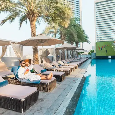 a man sitting on a chair next to a pool at a hotel at The First Collection Dubai Jumeirah Village Circle, a Tribute Portfolio Hotel in Dubai