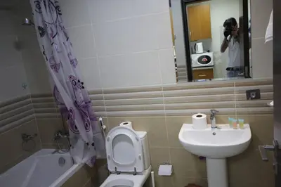 a person taking a picture of a bathroom with a toilet and sink at Cozy Rooms and Small Partitions for Men guests in Dubai in Dubai
