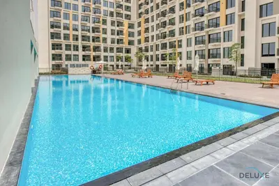 a large blue swimming pool with buildings in the background at Spotless 1BR at UNA Town Square Dubailand by Deluxe Holiday Homes in Dubai