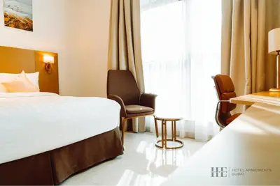 a hotel room with a bed and a chair and a window at HE Hotel Apartments in Dubai