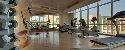 a gym with cardio equipment in a building with windows at Chelsea Gardens Hotel Apartment in Dubai