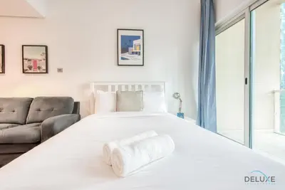 a large white bed in a room with a couch at Calm Studio at Lake View Tower JLT by Deluxe Holiday Homes in Dubai