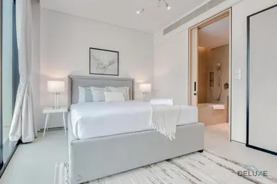 a white bedroom with a white bed and a bathroom at Modern 1BR Oasis in Prime Location, Book Now by Deluxe Holiday Homes in Dubai