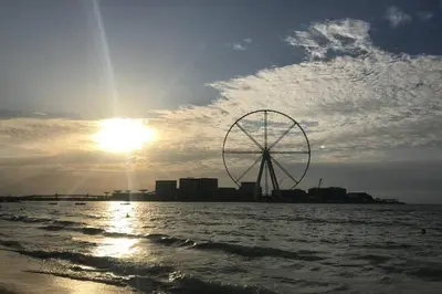a large ferris wheel on the beach with the sun at WSuites - Big Terrace with Beautiful Marina View in Dubai