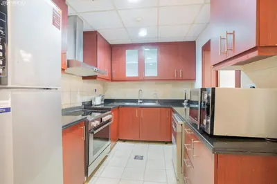 a kitchen with wooden cabinets and a stainless steel refrigerator at Gardenia Rimal Suites, Luxury Apartments in JBR with 2 min Walk to JBR beach in Dubai