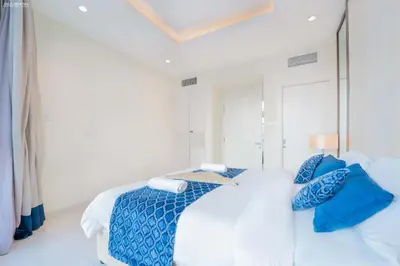 a white bedroom with a bed with blue pillows at Downtown Damac Distinction Full Burj View in Dubai