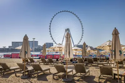 a beach with chairs and a ferris wheel in the background at Wonderful 2 Bedroom apartment in JBR in Dubai
