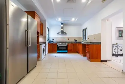 a large kitchen with wooden cabinets and a stainless steel refrigerator at Luxury Beachfront Villa with Direct Beach Access, Next to Community Pool, Close to the Thrills of Aquaventure Waterpark, Canal Cove, Palm Jumeirah by Deluxe Holiday Homes in Dubai