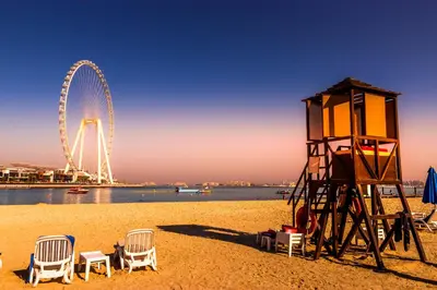a beach with chairs and a ferris wheel in the background at Brand New 5* Luxury Apartment in Address JBR in Dubai