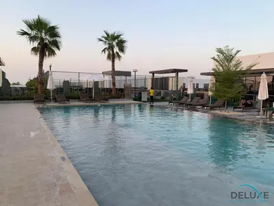 a large swimming pool with palm trees on a building at Extensive 3BR Townhouse at Janusia Damac Hills 2 by Deluxe Holiday Homes in Dubai