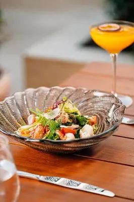 a salad in a glass bowl on a table with a drink at The Dubai EDITION in Dubai
