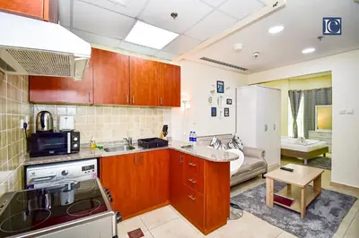 a kitchen with wooden cabinets and a living room at Luxury Escapes - Budget Studio - New Dubai Gate 2 JLT in Dubai