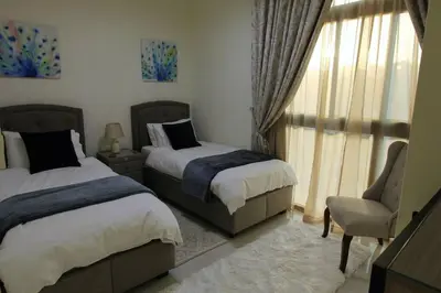 a bedroom with two beds and a chair and a window at Upgraded spacious 3BR+Maid Villa in Dubai