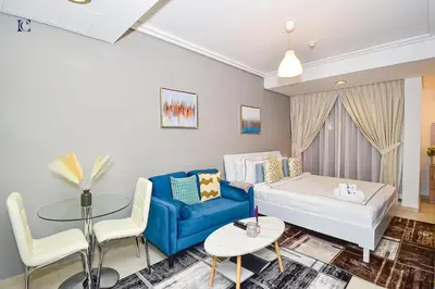 a living room with a blue couch and a table at Luxury Escapes - Cozy Studio with Balcony near Metro - Goldcrest 2 JLT in Dubai