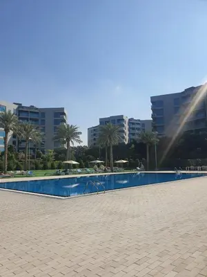 a large swimming pool with palm trees and buildings at Cozy 1-bedroom apartment in Dubai South with Pool in Dubai