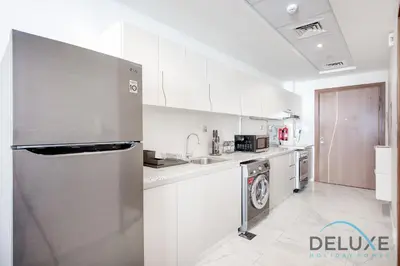 a kitchen with white cabinets and a stainless steel refrigerator at Intimate Studio at Millennium Binghatti Residence Business Bay by Deluxe Holiday Homes in Dubai