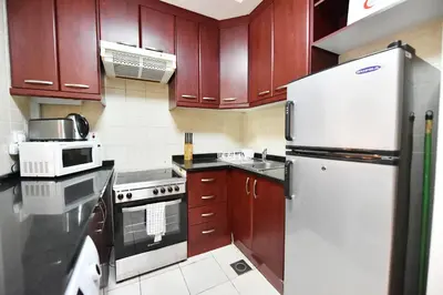 a kitchen with wooden cabinets and a white refrigerator at Luxury Escapes - Spacious Fully Furnished Studio Apt - Next to Metro, 5 Mins from Mall - MED46 in Dubai