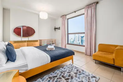 a bedroom with a bed and a chair and a window at Lovely 2-bed condo in JBR - 5 mins from beach - Palm View! in Dubai