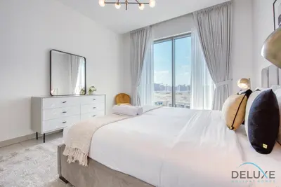 a white bedroom with a large bed and a window at Notable 2BR at Sobha Hartland Greens MBR City by Deluxe Holiday Homes in Dubai