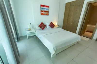 a white bedroom with a bed and a night stand at Deluxe One Bedroom Apartment for rent in Dubai Al Barsha south in Dubai