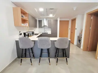 a kitchen with three bar stools at a kitchen counter at Modern 1BR in Jumeirah Village Circle (Pool View) in Dubai