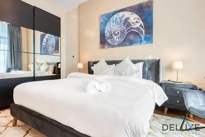 a bedroom with a white bed and a painting on the wall at Short Distance from Global Village & Other Major Attractions Studio Unit, Al Jawhara Tower, Jumeirah Village Triangle by Deluxe Holiday Homes in Dubai