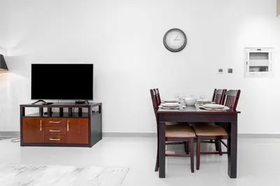 a dining room with a table with a tv and a clock at White Sage - Elite Residence 1 bedroom in Dubai