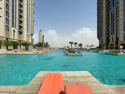 a large swimming pool with orange chairs and buildings at The Smart Concierge - Amna Tower in Dubai