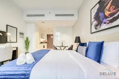a large white bed with blue sheets in a bedroom at Sunlit Studio at Golf Promenade 2A DAMAC Hills By Deluxe Holiday Homes in Dubai