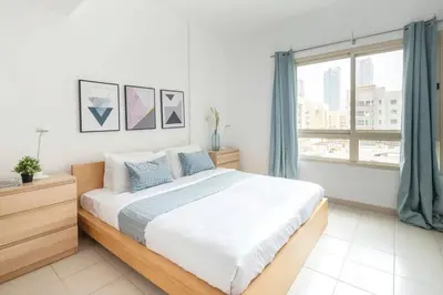 a white bedroom with a large bed and a window at Frank Porter - Al Samar in Dubai