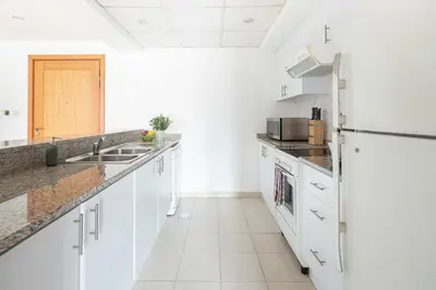 a white kitchen with a sink and a refrigerator at Frank Porter - Al Samar in Dubai