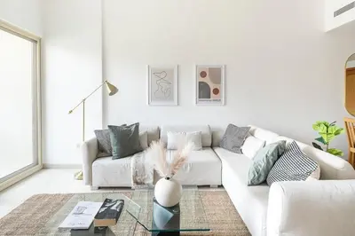 a white living room with a white couch and a table at Frank Porter - Al Samar in Dubai