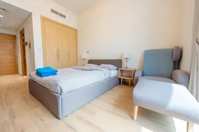 a bedroom with two beds and a blue chair at Luxury Escapes - Cozy Studio In front of Metro Stn - Access to Gym & Pool - Aura Azizi in Dubai