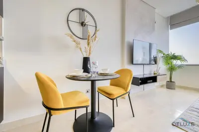 a dining room with yellow chairs and a table and a tv at Affordable Luxury Modern 1BR with Pool & Balcony by Deluxe Holiday Homes in Dubai