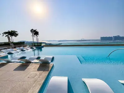 a swimming pool with white lounge chairs and the ocean at HiGuests - Superlative apt with private beach access in Dubai